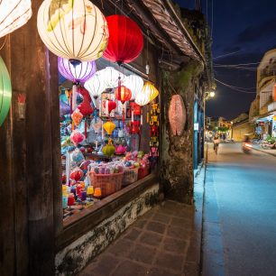 18533300 - wide view on narrow street in hoi an town in vietnam and shop on left with big bright window and multicolored lanterns over it  houses going into distance on right  travelling and tourism