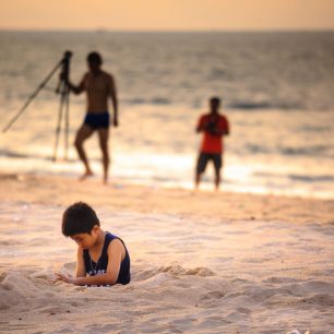 41298089 - vung tau vietnam may 16 2015: a young boy unknown sitting alone on the beach with sand vi thinking is far behind look like the two men holding the image capture device