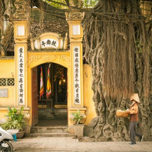 43486652 - hanoi, vietnam - april 25, 2014: vietnamese woman in conical hat with basket in hands is passing by the temple on the street of old quarter, hanoi, vietnam on april 25, 2014.
